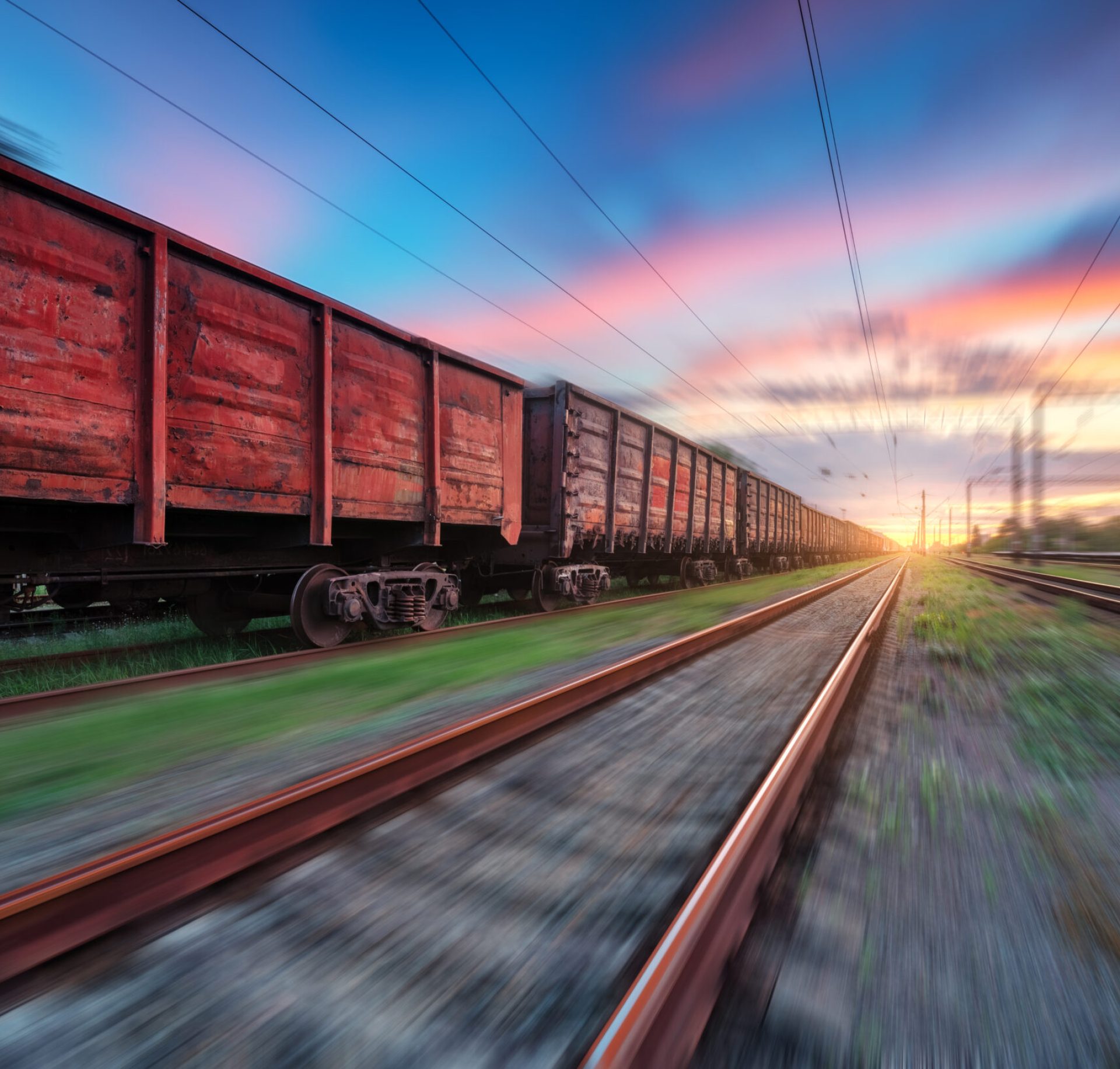 Moving freight train at sunset. Railroad and beautiful sky with clouds with motion blur effect in summer. Industrial landscape with train, railway station and blurred background.  Railway platform