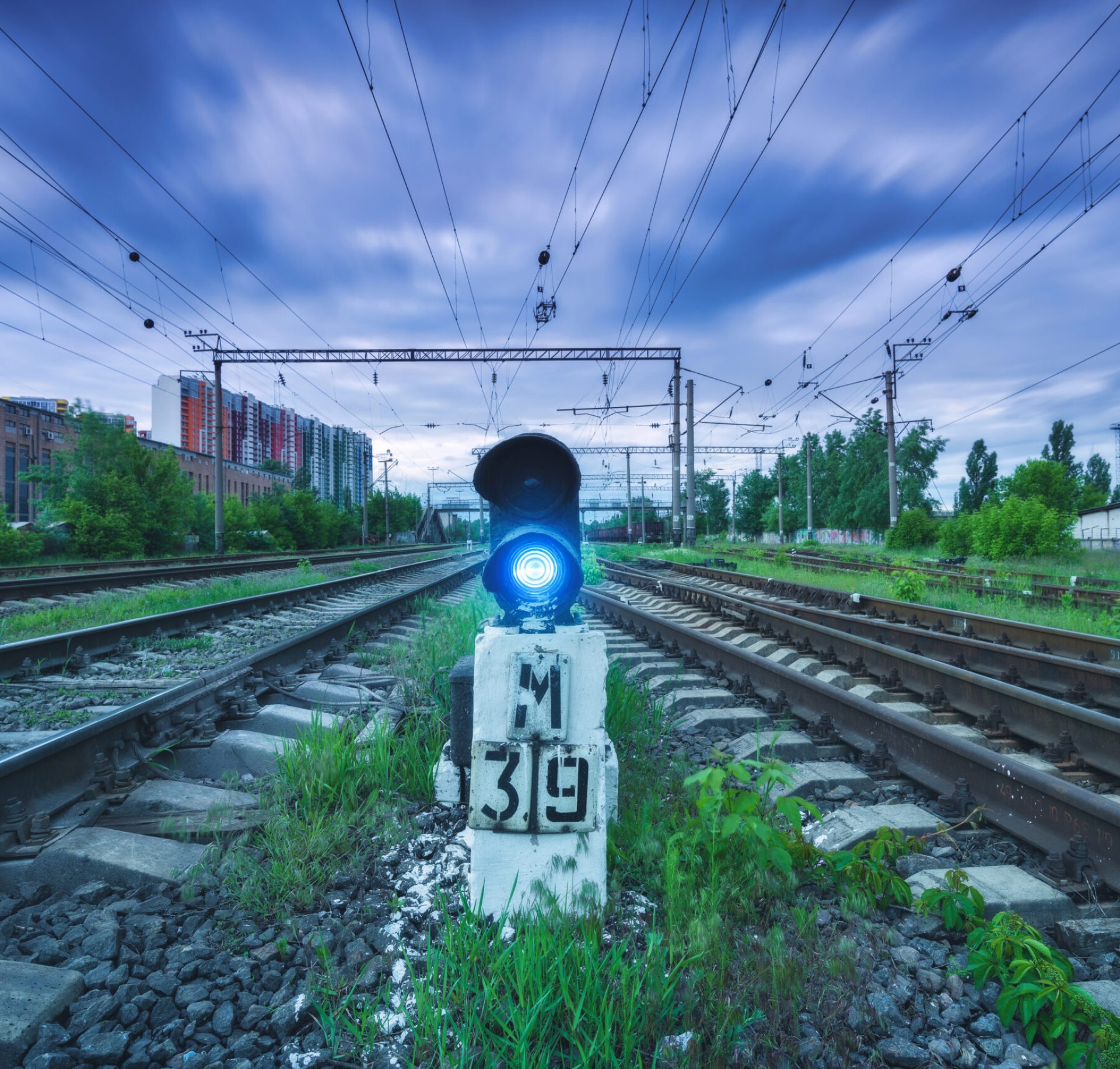 Railway station with traffic light and blurred sky with clouds at sunset. Dramatic industrial landscape with railroad. Railway platform with semaphore with blue light. Heavy industry. Transportation