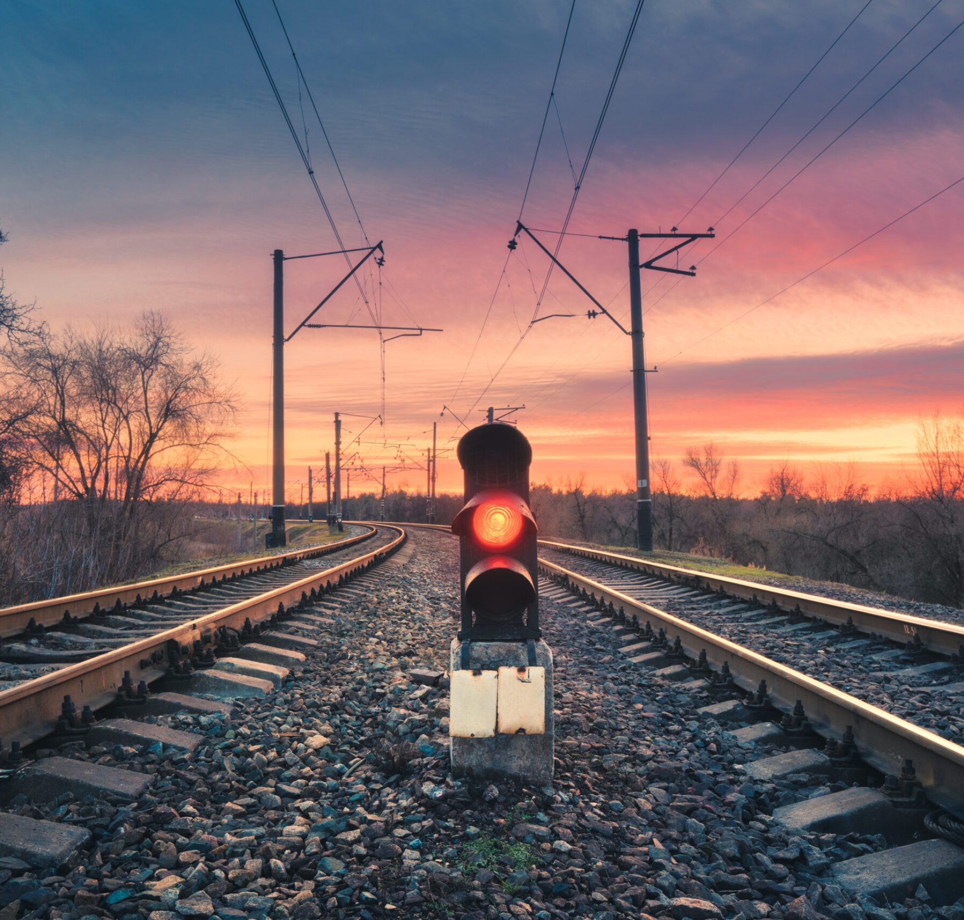 Railway station with semaphore against sunny sky with clouds at sunset. Colorful industrial landscape. Railroad. Railway platform with traffic light in the evening. Heavy industry. Cargo shipping