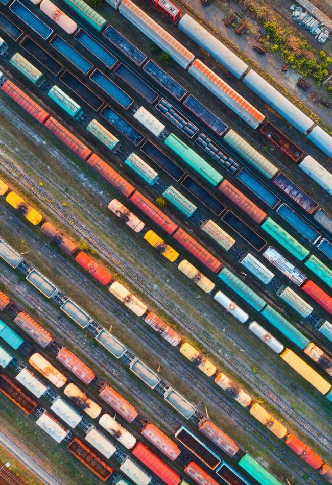 Top view of colorful cargo trains. Aerial view from flying drone of colorful freight trains on the railway station. Wagons with goods on railroad. Heavy industry. Industrial conceptual scene